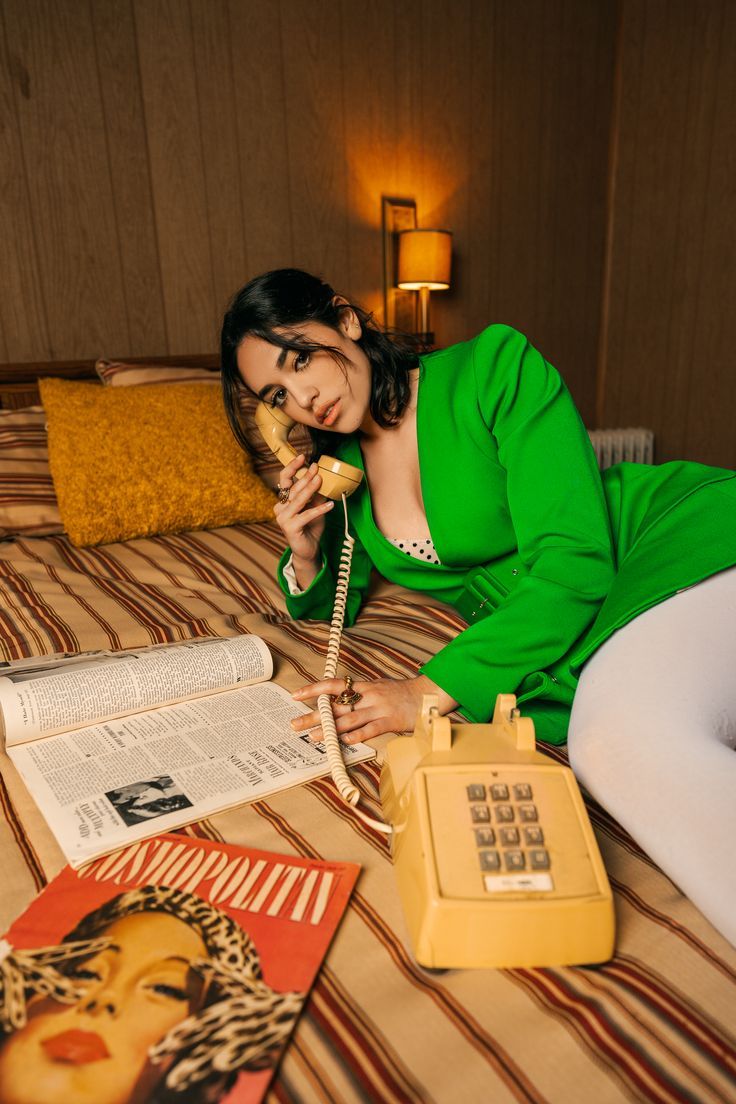 a woman laying on top of a bed next to an old fashioned telephone and magazine