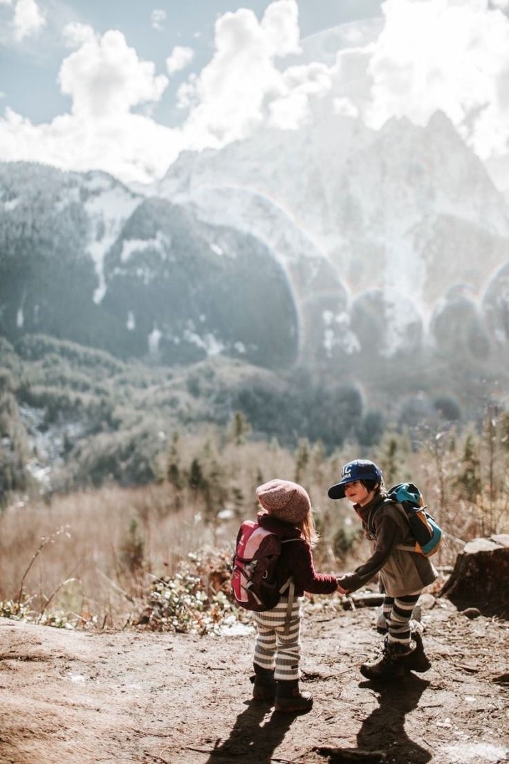 two young children holding hands on top of a dirt hill with mountains in the background