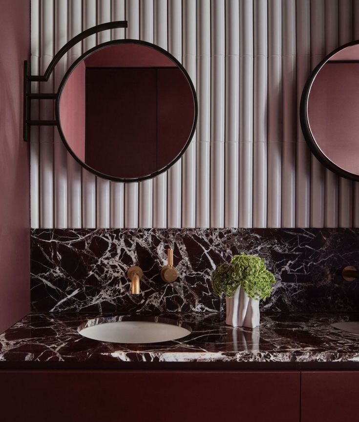 a bathroom with two round mirrors above the sink and marble counter top, along with a vase filled with flowers