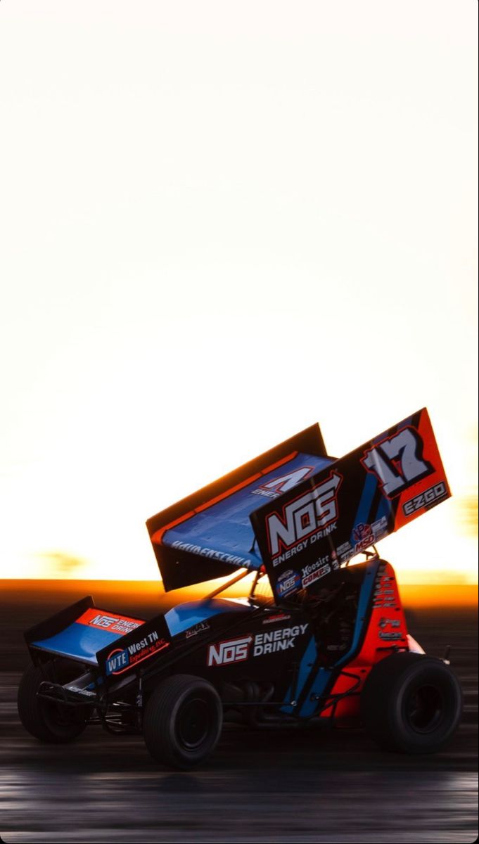 a person driving a race car on a track with the sun setting in the background