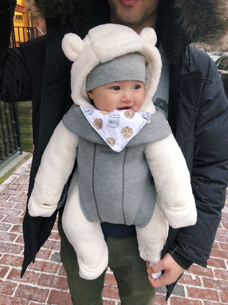 a man is holding a baby wearing a bear costume on his chest while he wears a bib