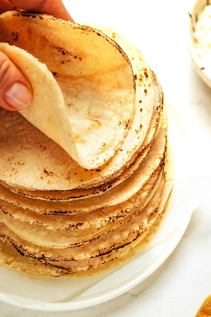 a stack of tortillas on a plate being held by a person's hand