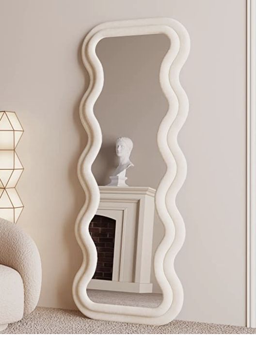 a large white mirror sitting on top of a floor next to a chair and fireplace