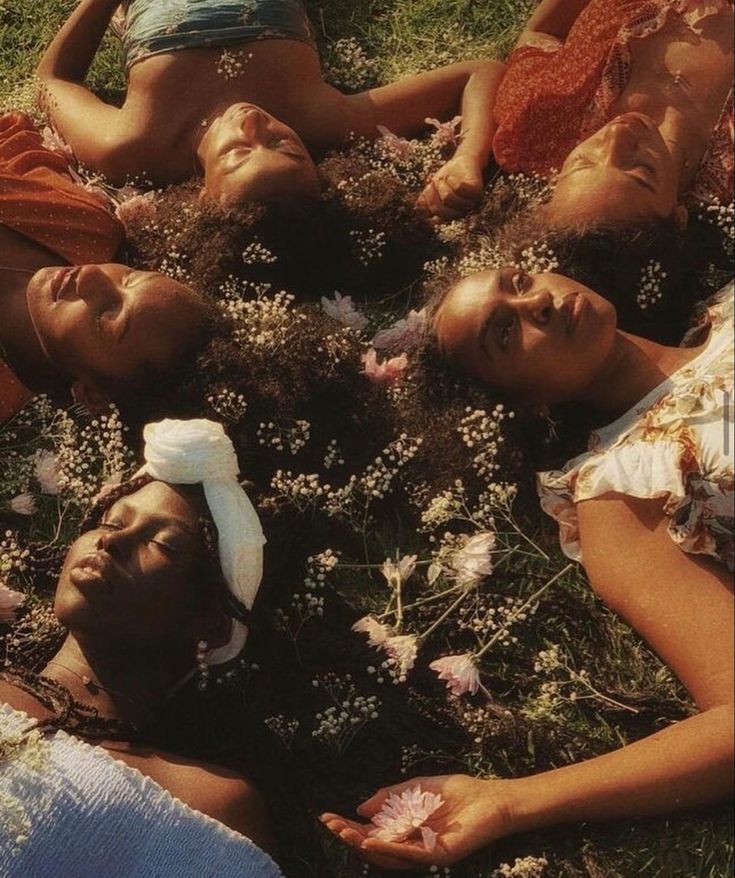 four women laying on the grass with flowers in their hair and wearing headbands