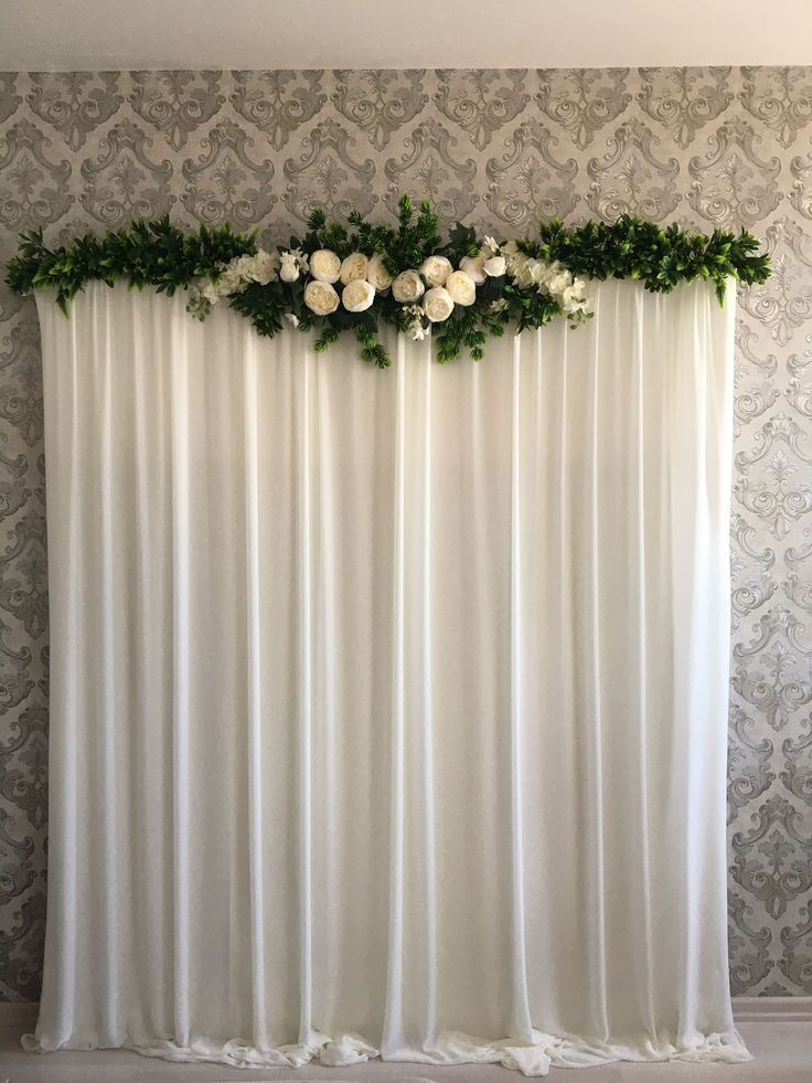 white flowers and greenery decorate the top of a curtain in front of a wall