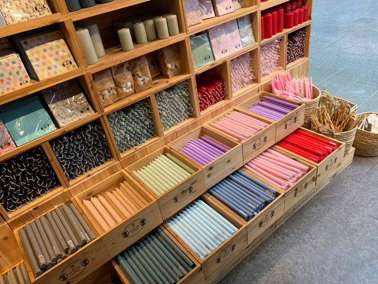 many different colored candles are on display in a wooden case and some baskets with straws