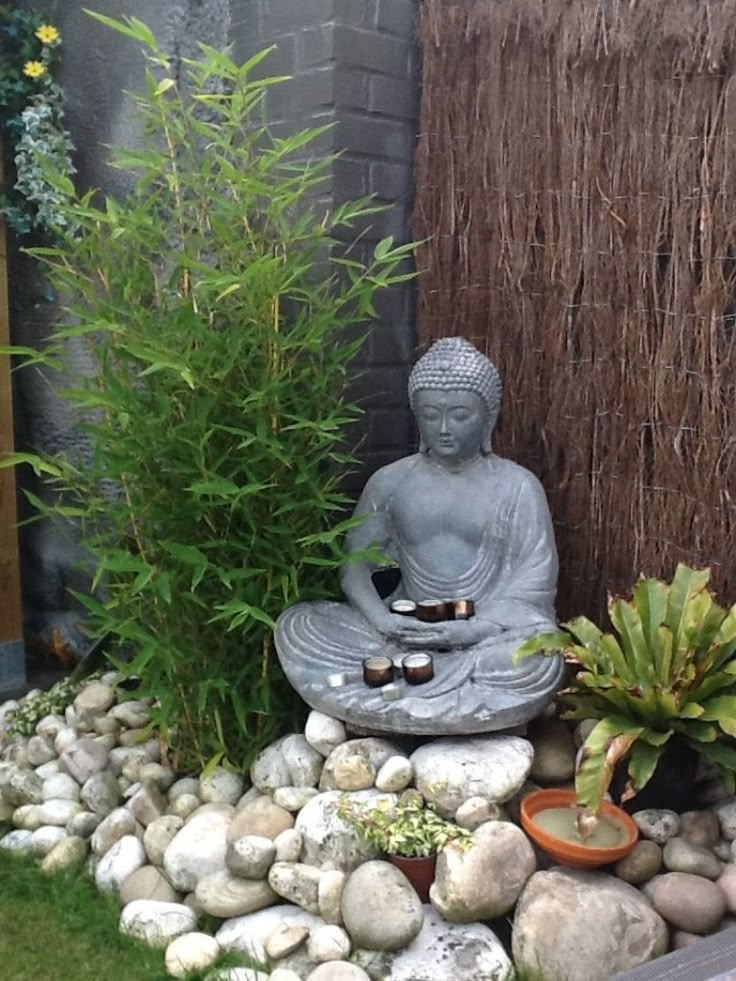 a buddha statue sitting on top of a pile of rocks next to a planter