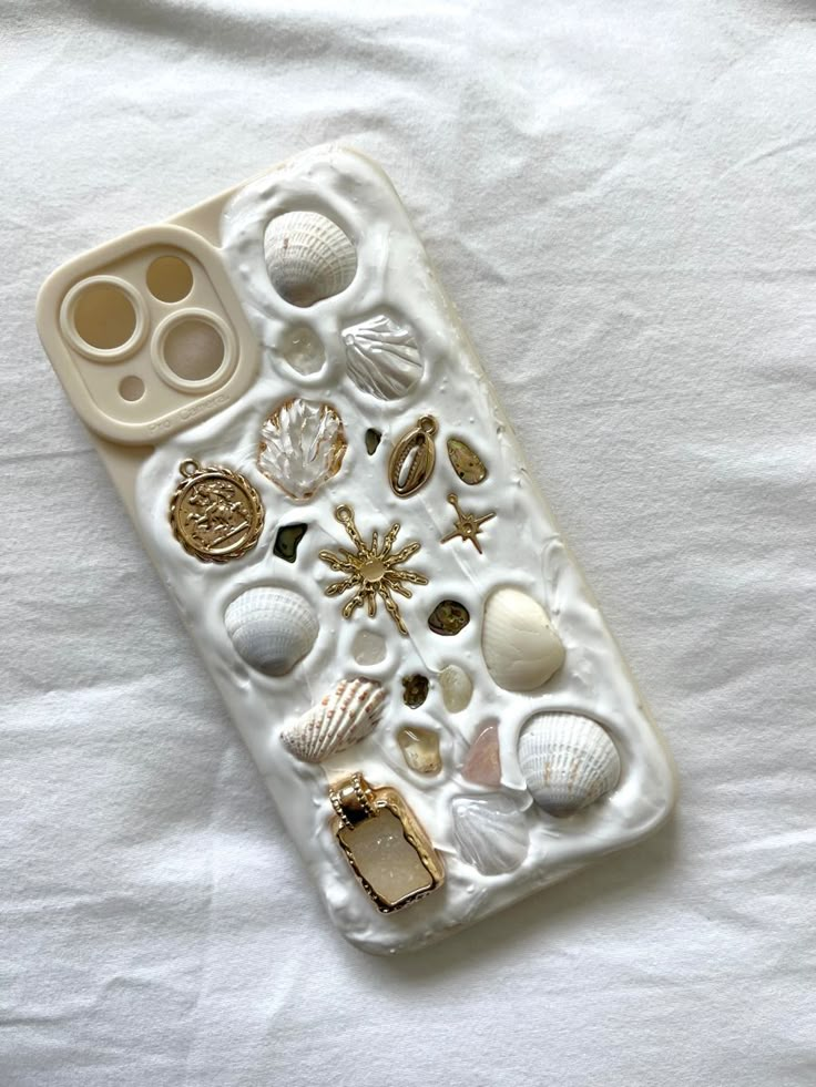 an iphone case with shells and seashells on it sitting on a white sheet