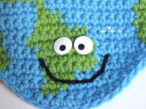 a crocheted blue and green bag with a smiling face