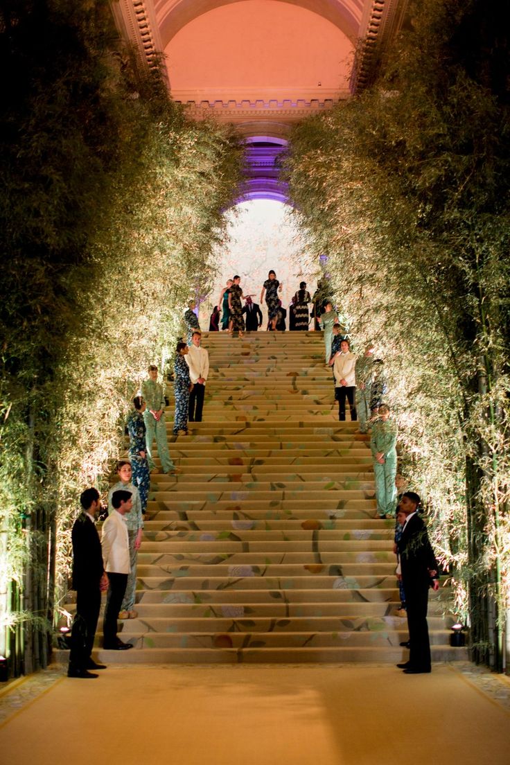 people are standing on the stairs in front of trees and flowers at night time,