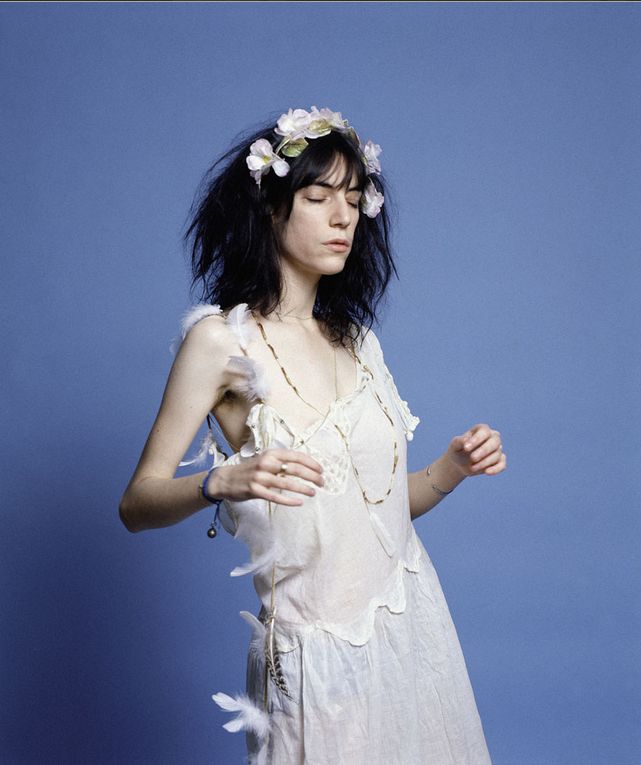 a woman in a white dress with feathers around her neck and headband, standing against a blue background