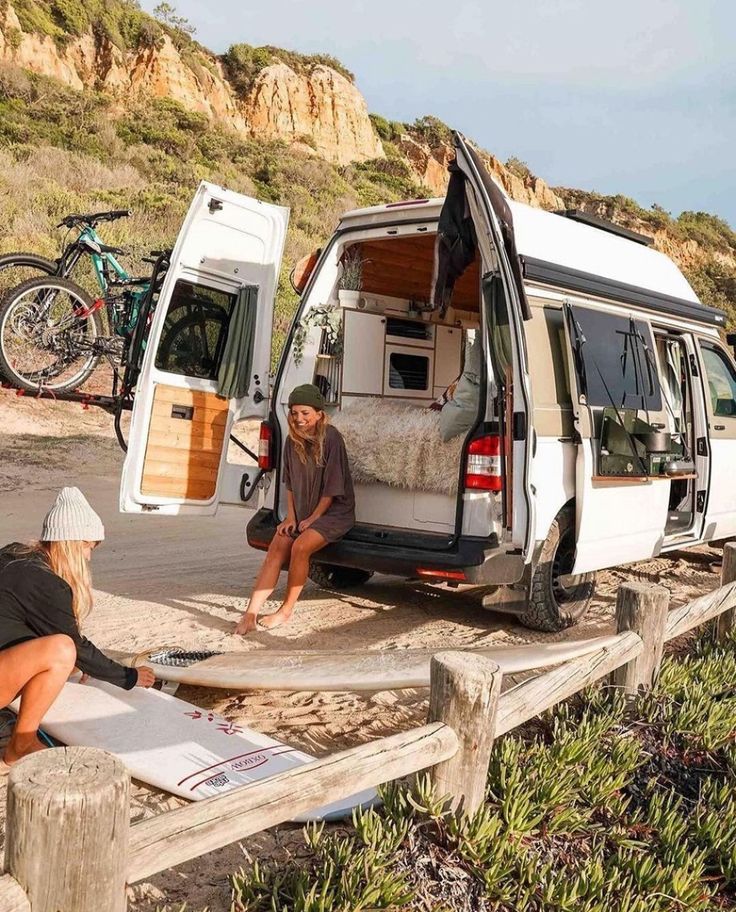 two people sitting in the back of a van with their surfboards on the beach