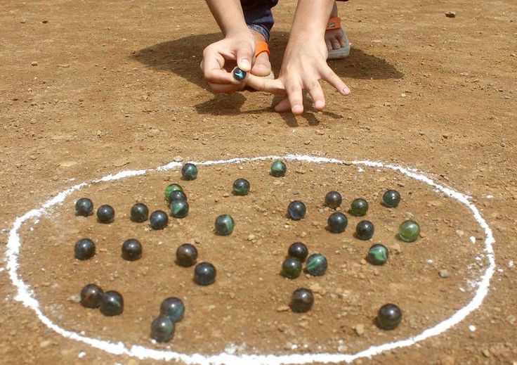 a young boy is playing with balls in the dirt and on the ground, while his hands are pointing at them