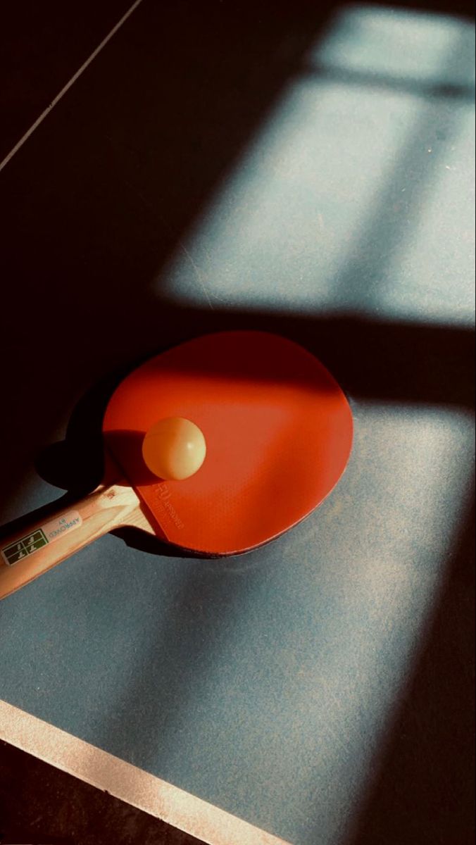 an orange ping pong paddle resting on top of a wooden table next to a window