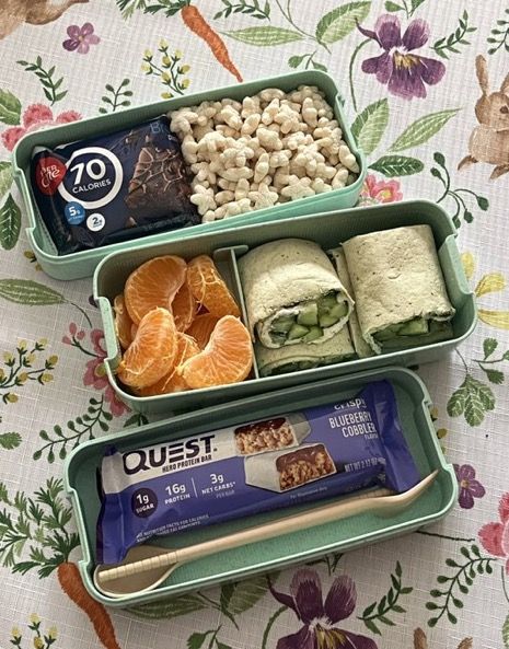 two bento boxes filled with food on top of a floral tablecloth covered table