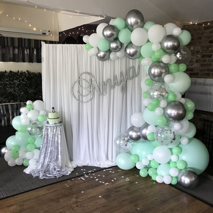 an arch made out of balloons and streamers with a cake on the table next to it