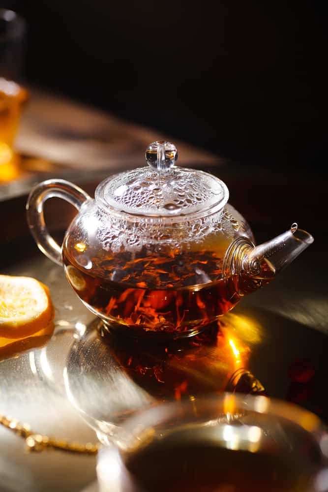 a glass tea pot filled with liquid next to slices of lemon on a table top