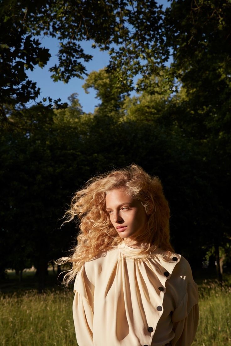 a woman standing in the grass with her hair blowing back and looking off to the side