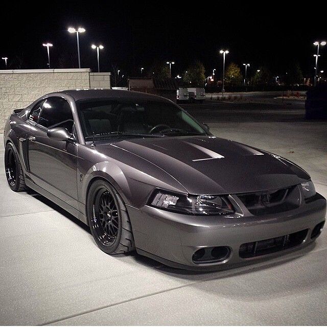 a silver sports car parked in a parking lot at night with street lights behind it