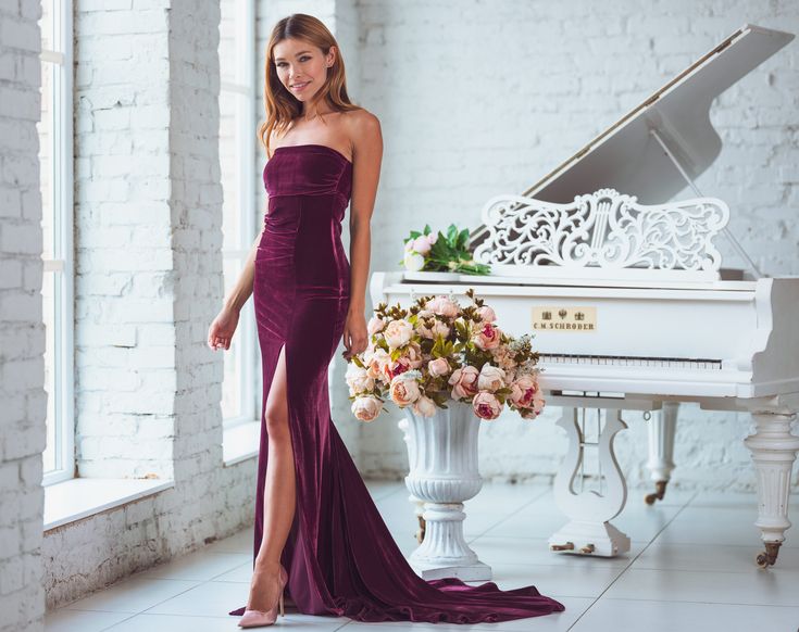 a woman standing in front of a piano wearing a purple dress and holding a bouquet