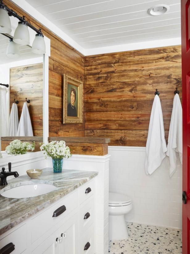 a bathroom with wood paneling and white fixtures is pictured in this image, there are two towels hanging on the wall