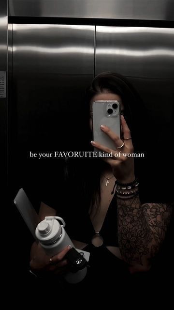 a woman taking a selfie with her cell phone in an elevator stall while holding a camera