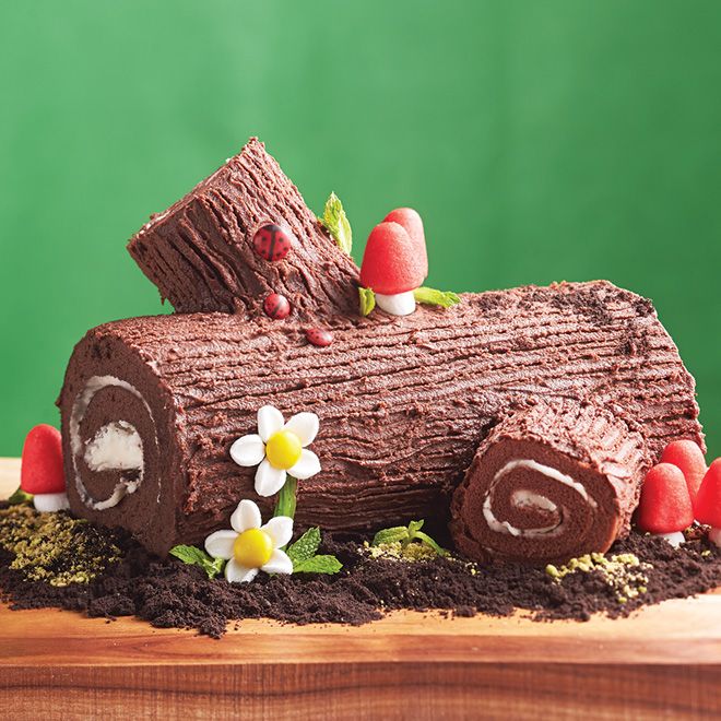 a cake made to look like a log with flowers and leaves around it on a wooden table