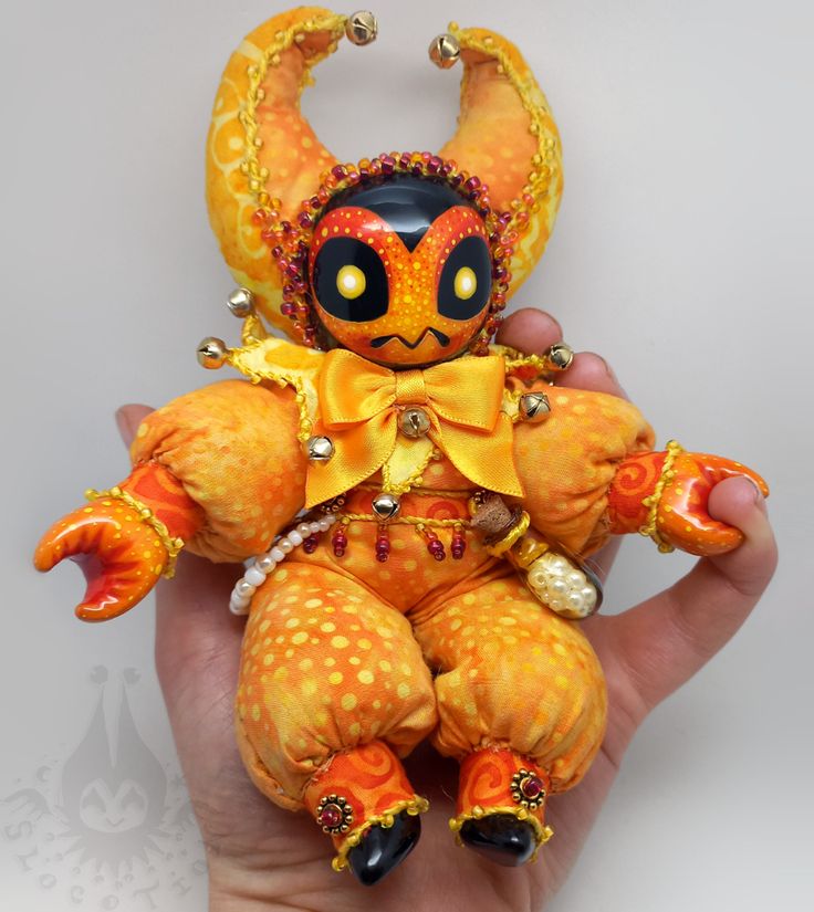 a hand holding an orange and yellow stuffed animal with horns on it's head