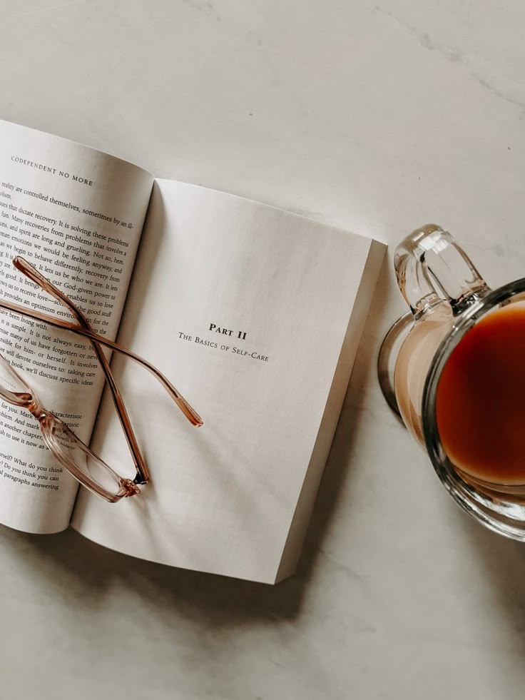 an open book with glasses on top of it next to a cup of tea or coffee