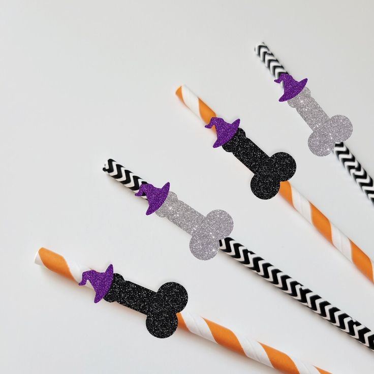 three mickey mouse straws with purple and black bows on them, sitting next to orange and white striped straws