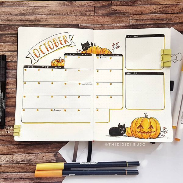 an open planner with pumpkins and black cats on it, next to some pens