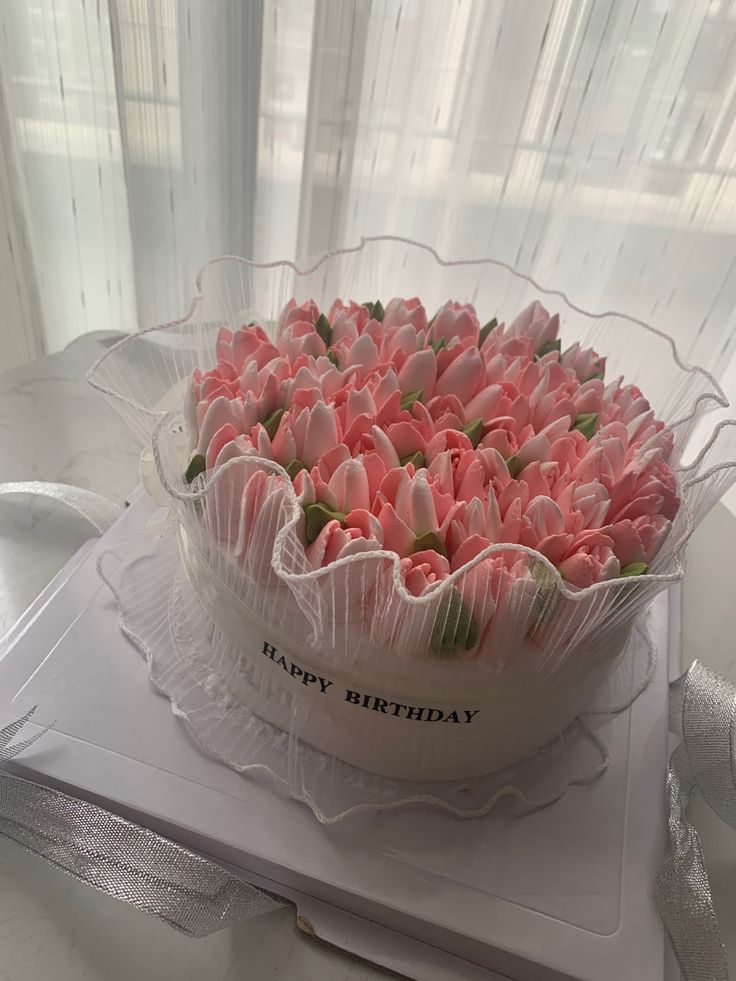 a birthday cake with pink tulips in a clear plastic container on a table