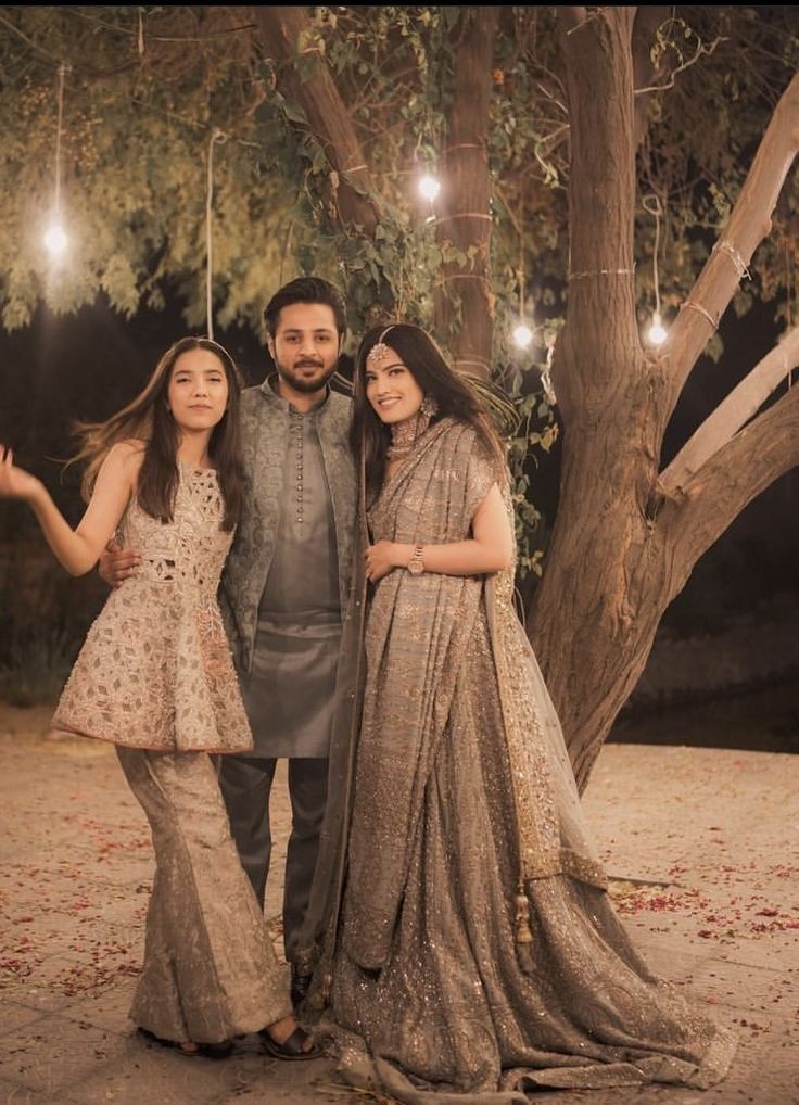 two women and a man posing for a photo under a tree with lights strung from the branches