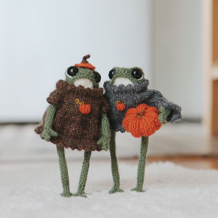 two knitted frog figurines standing next to each other on a white carpet