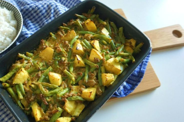 a pan filled with green beans and rice next to a wooden spatula on top of a blue towel