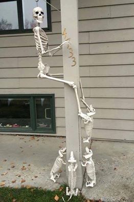 a pole with skeletons hanging from it's side on the sidewalk in front of a house