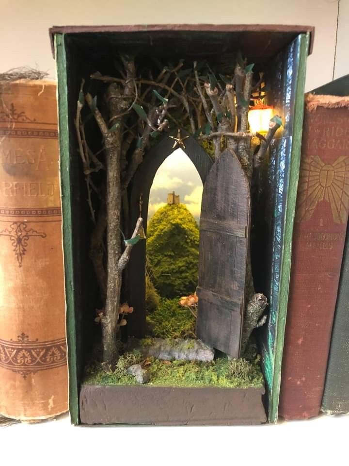 an open book case with trees and moss in the middle, sitting on a shelf next to two books