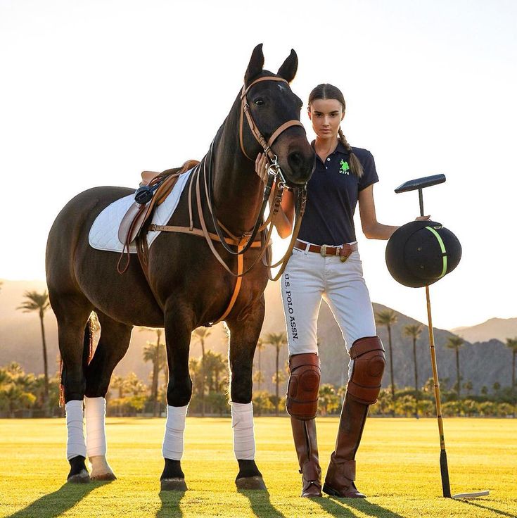 a woman standing next to a brown horse on top of a lush green field with palm trees in the background