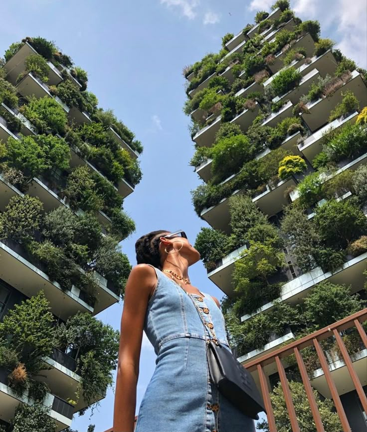 a woman standing in front of a tall building with plants growing on it