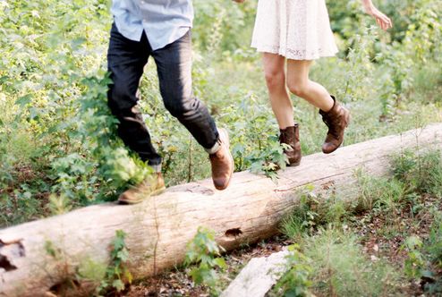 a man and woman walking on a log in the woods