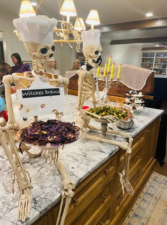 two skeletons sitting on top of a counter in a kitchen next to a bowl of food