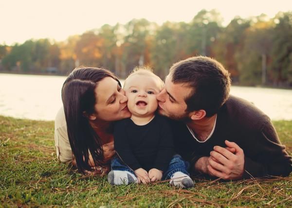 a couple kissing their baby while laying on the grass