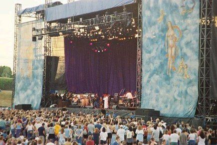 a large group of people standing on top of a stage next to a giant blue curtain