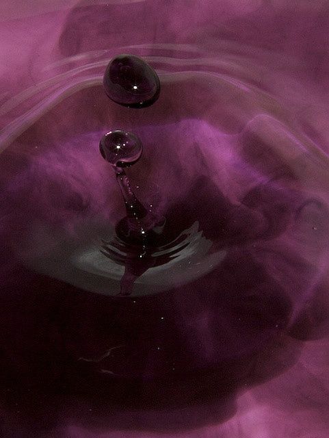 a water drop that is in some kind of bowl with purple and black liquid around it