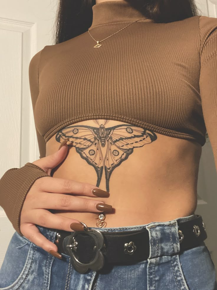 a woman with a butterfly tattoo on her stomach, wearing jeans and a brown top