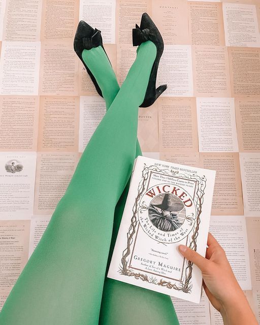 a person wearing green stockings and black shoes laying on top of a book with her legs crossed