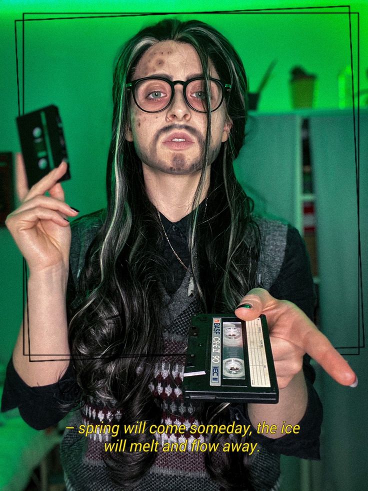 a man with long hair and glasses holding a cell phone in one hand and pointing to the other