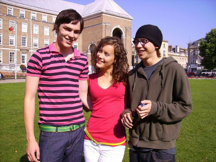 three young people standing next to each other in front of a building with a clock tower