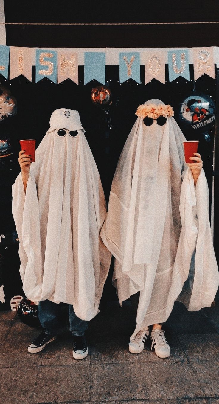 two people dressed up in ghost costumes holding drinks