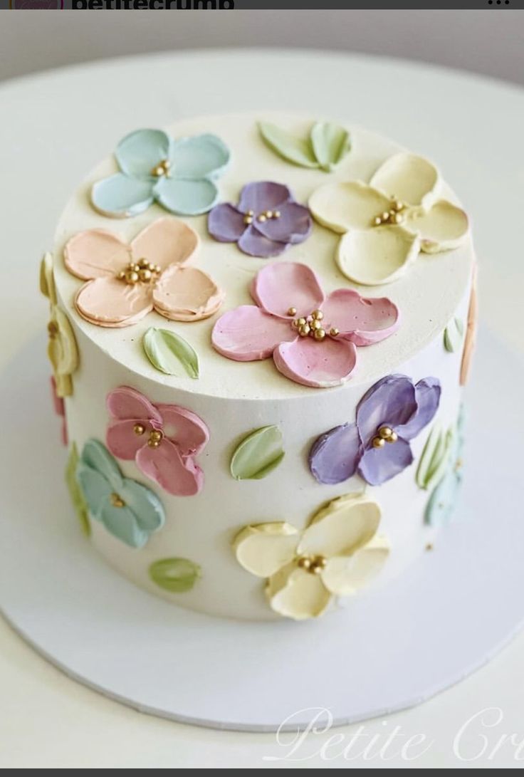 a white cake with colorful flowers on it's side and the top layer is covered in fondant